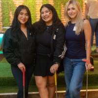 Three women holding golf clubs and smiling at camera